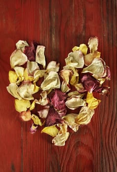 Beautiful heart shape made with pink , red , yellow petals on red wooden table