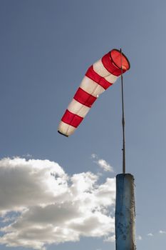 A windsock on flagpole against blue cloudy sky white and red striped conical textile tube 