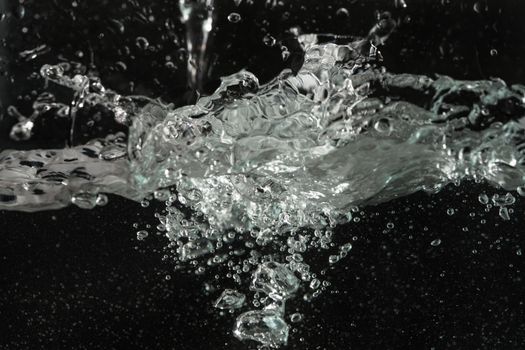 Water splashing as it's poured into aquarium tank, black background.