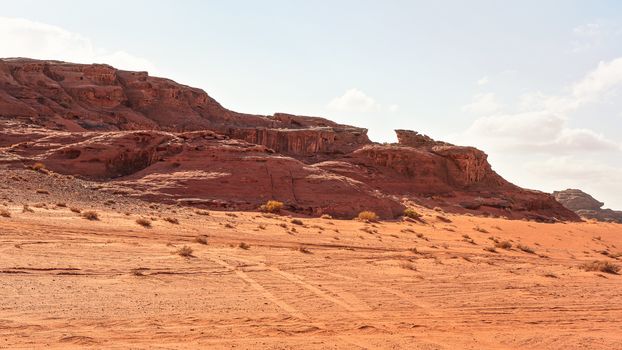 Rocky massifs on red sand desert, bright cloudy sky in background - typical scenery in Wadi Rum, Jordan.