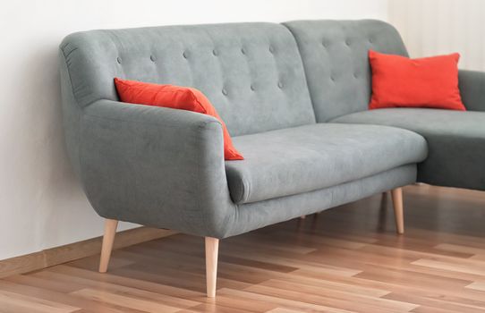 Modern gray couch with red pillows on wooden tiled floor - office furniture.