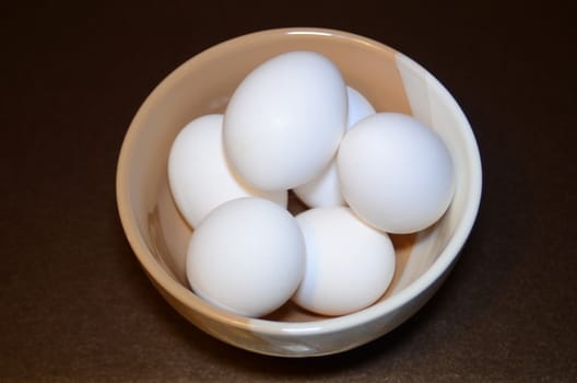 white chicken eggs in a two-color bowl located on a dark background