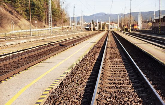 Empty train station in small city on sunny day, shallow depth of field photo, focus on concrete platform and steel rails foreground.