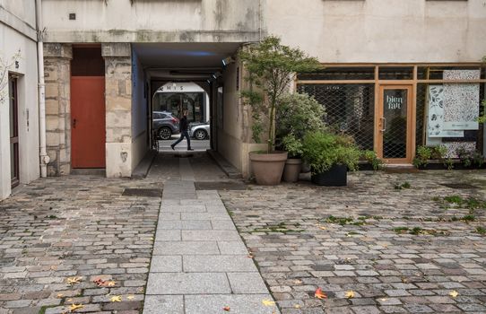 Paris, France -- November 4, 2017. A wide angle lens captures a  pedestrian looking into a courtyard as he walks by.