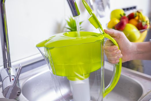 Woman filling water filter jug in the kitchen. Purification and softening of drinking tap water. Closeup