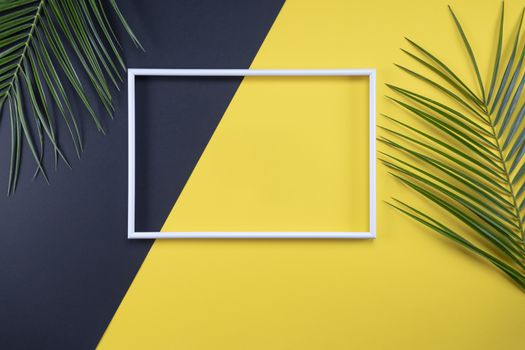 Summer composition with photo frame and green leaves on yellow background. Creative mockup with copy space and tropical leaves.