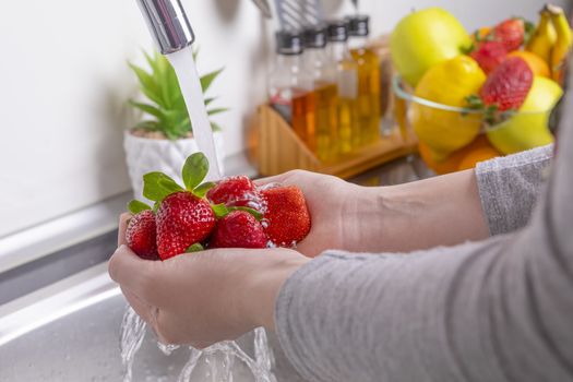 Woman hands washing strawberries in the kitchen. Eating fresh and healthy fruits concept. Closeup