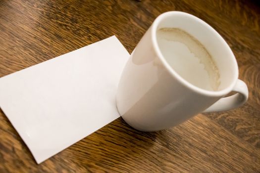 Empty coffee cup with empty bill, receipt on wooden table. Cafe or restaurant.