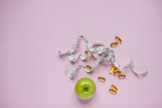 Diet and healthy eating concept. Top view of weightloss. Measuring tape and capsules and diet pills and green apple. Lilac background