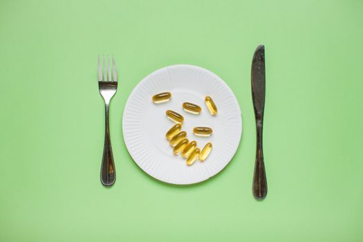 Diet and healthy eating concept. Top view of weightloss. knife with a fork, capsules, tablets. Green background