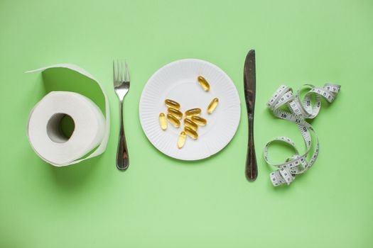 Diet and healthy eating concept. Top view of weightloss. Green apple, measuring tape, knife with a fork, capsules, tablets, toilet paper. Green background