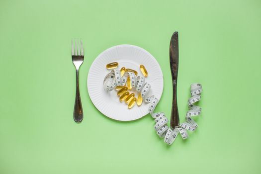 Diet and healthy eating concept. Top view of weightloss. measuring tape, knife with a fork, capsules, tablets. Green background