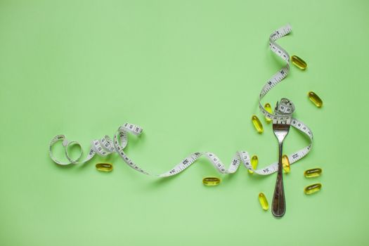 Diet and healthy eating concept. Top view of weightloss. Measuring tape on a fork. Capsules and diet pills. Green background