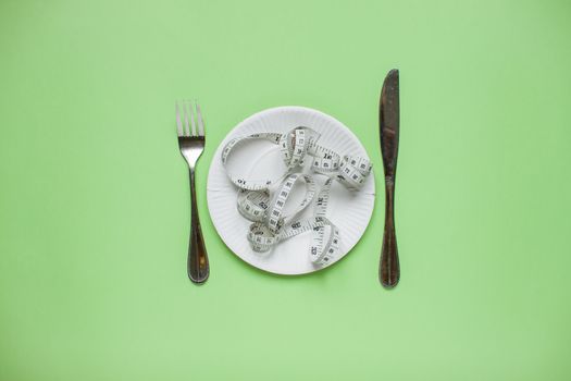 Diet and healthy eating concept. Top view of weightloss. Measuring tape on a plate, knife with a fork. Green background