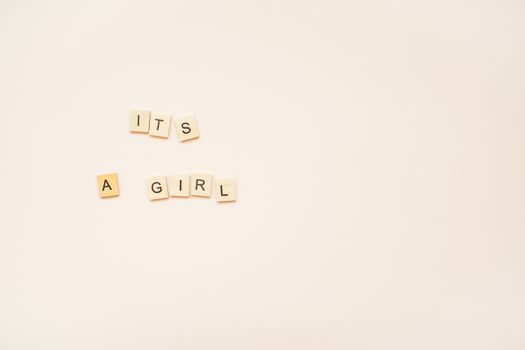 The inscription "It's a girl" from wooden blocks on a light pink background.