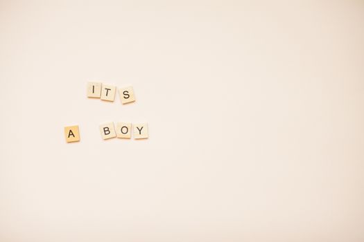 The inscription "It's a boy" from wooden blocks on a light pink background.