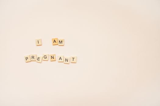 The inscription "I am pregnant" made of wooden blocks on a light pink background.