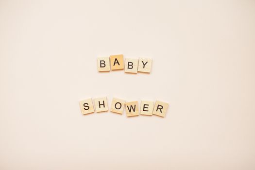 The inscription "baby shower" made of wooden blocks on a light pink background.