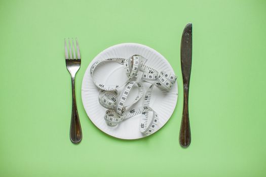 Diet and healthy eating concept. Top view of weightloss. Measuring tape on a plate, knife with a fork. Green background