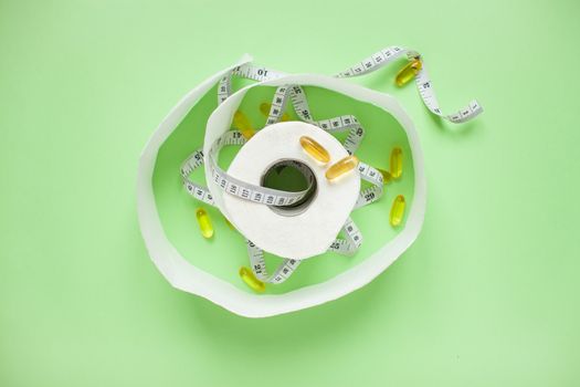 Diet and healthy eating concept. Top view of weightloss. Measuring tape and toilet paper. Capsules and diet pills. Green background