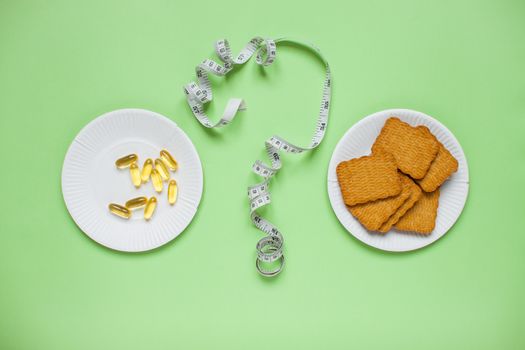 Diet and healthy eating concept. Top view of weightloss. Choose between diet pills and cookies. Question mark from a measuring tape. Green background