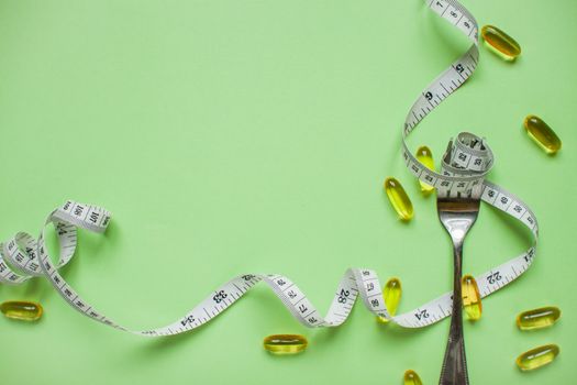 Diet and healthy eating concept. Top view of weightloss. Measuring tape on a fork. Capsules and diet pills. Green background