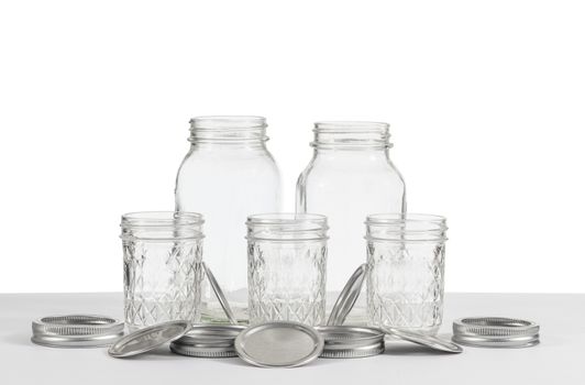 Horizontal shot of a group of old canning jars of two different sizes with rings and lids on a white background.