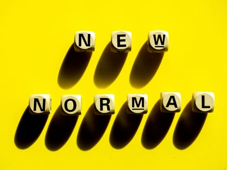 NEW NORMAL, word on wooden alphabet cube on yellow background, top view, minimal style. New normal after covid-19 pandemic with social distancing concept.