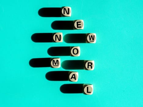 NEW NORMAL, word on wooden alphabet cube on light green background, top view, minimal style. New normal after covid-19 pandemic with social distancing concept.