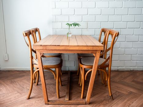 Wooden dining table and four chairs with green leaf in glass vase on white wall background in restaurant.