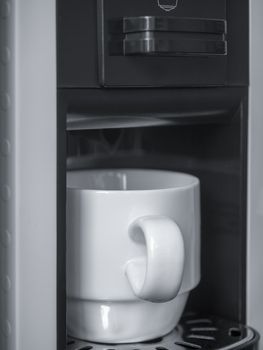 White ceramic coffee cup on coffee machine, vertical style.