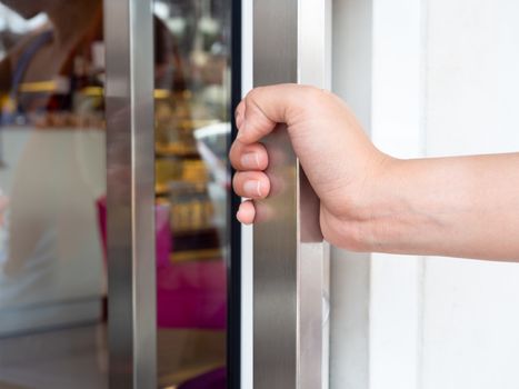 Close-up hand takes aluminium handle on glass door for open the door.