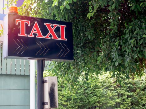 Taxi calling sign with red flashing emergency light for residents in village on green tree background with copy space.