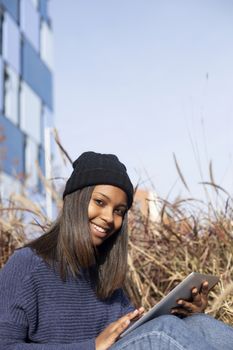 Portrait of African American young woman wearing a wool cap standing on the street while using a mobile phone