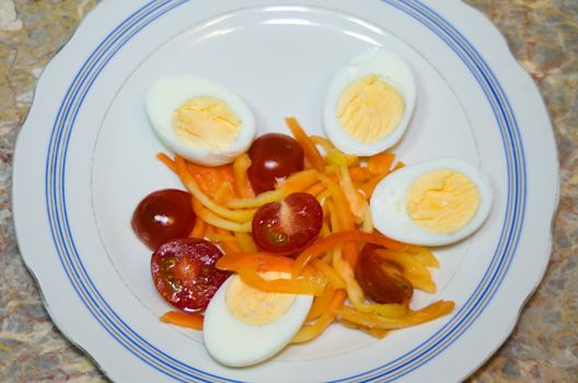 simple food on a light plate - vegetables and chicken eggs: cherry tomatoes, bell peppers in the form of straw and halves of chicken eggs