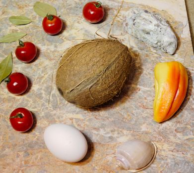 vegetables, fruits, seashells and an egg on a marble surface: cherry tomatoes, bell peppers, bay leaves, oyster, shell, coconut and chicken egg