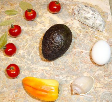 vegetables, seashells, egg and avocado on a marble surface: cherry tomatoes, bell peppers, bay leaves, oyster, shell, chicken egg and avocado