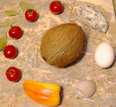 vegetables, seashells, egg and coconut on a marble surface: cherry tomatoes, bell peppers, bay leaves, oyster, shell, chicken egg and coconut