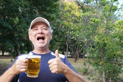 a laughing man holds a mug of beer in one hand, with the other hand shows that everything is fine in the park