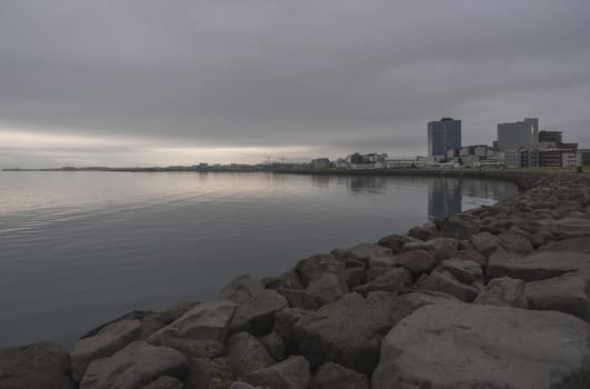 Seascape with stone coast in reykjavik, iceland. City building on sea side. Skyline on cloudy sky. Architecture and construction. Early morning, mooody sky