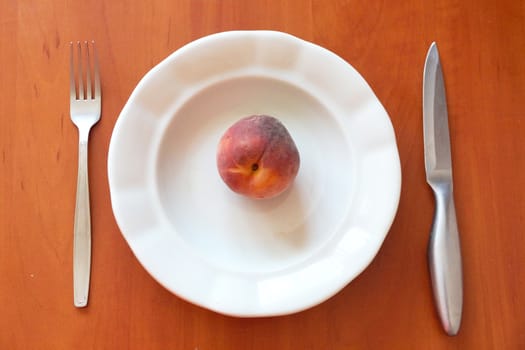 one peach on an empty white plate and cutlery nearby, healthy eating concept, view from above