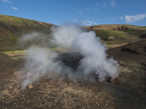 Hot spring with boiling water rising from rocks in Landmannalaugar colorful Rhyolit mountains on famous Laugavegur trek. Fjallabak Nature Reserve in Highlands of Iceland.