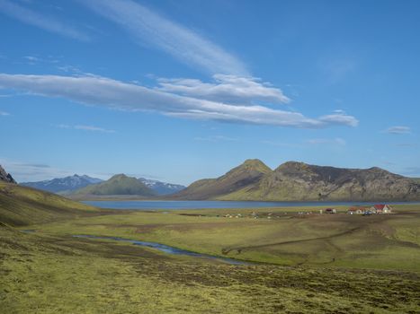 Colorful tents at camping site on blue Alftavatn lake with green hills and glacier in the otherwordly beautiful landscape of the Fjallabak Nature Reserve in the Highlands of Iceland. Part of famous Laugavegur hiking trail.