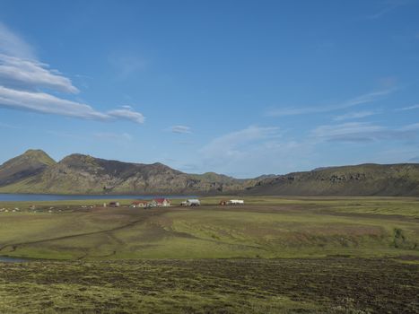 Panoramic landscape with mountain huts at camping site on blue Alftavatn lake with river, green hills and glacier in beautiful landscape of the Fjallabak Nature Reserve in the Highlands of Iceland part of Laugavegur hiking trail