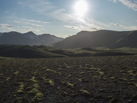 Volcanic landscape with snow covered mountains, green hills and lava gravel ground covered by lush moss. Fjallabak Nature Reserve in the Highlands of Iceland.
