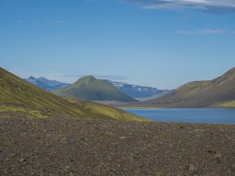 Beautiful landscape of blue Alftavatn lake with snow covered mountains and green hills and blue sky background. Summer landscape of the Fjallabak Nature Reserve in the Highlands of Iceland. Copy space