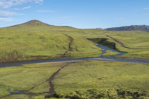 Group of hikers preparing to ford across the blue river stream at Laugavegur hiking trail. Landscape with green hills, meadow and lush moss. Fjallabak Nature Reserve, Iceland. Summer blue sky.