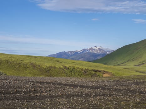 Volcanic landscape with snow-capped mountains of Tindfjallajokull glacier massif, green hills and lava gravel ground covered by lush moss. Fjallabak Nature Reserve in the Highlands of Iceland.