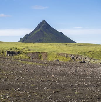 Volcanic landscape with green Storasula mountain, hills and lava gravel ground covered by lush moss. Fjallabak Nature Reserve in the Highlands of Iceland.