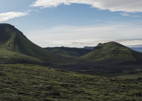 Volcanic landscape with blue container,Tindfjallajokull glacier, green hills and lava gravel ground covered by grass and moss. Fjallabak Nature Reserve, Iceland.